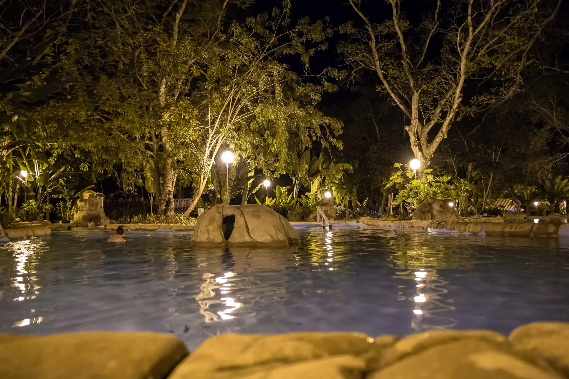 Piscina principal do Parque das Águas Quentes à noite, iluminada por luzes amarelas refletidas na água