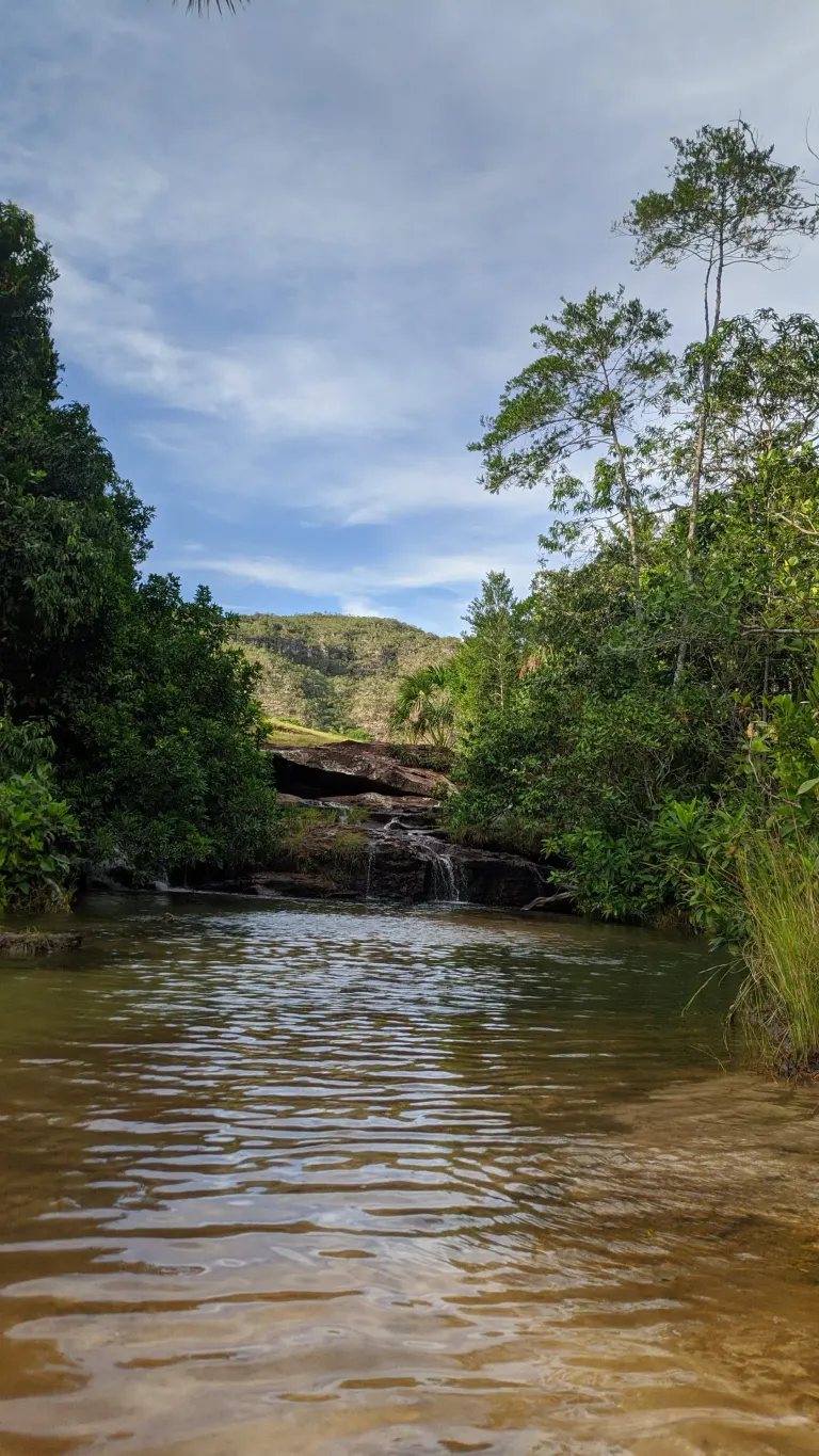Poço de água da Cachoeira do Paraíso com pequena queda e a serra ao fundo, cercado de mata