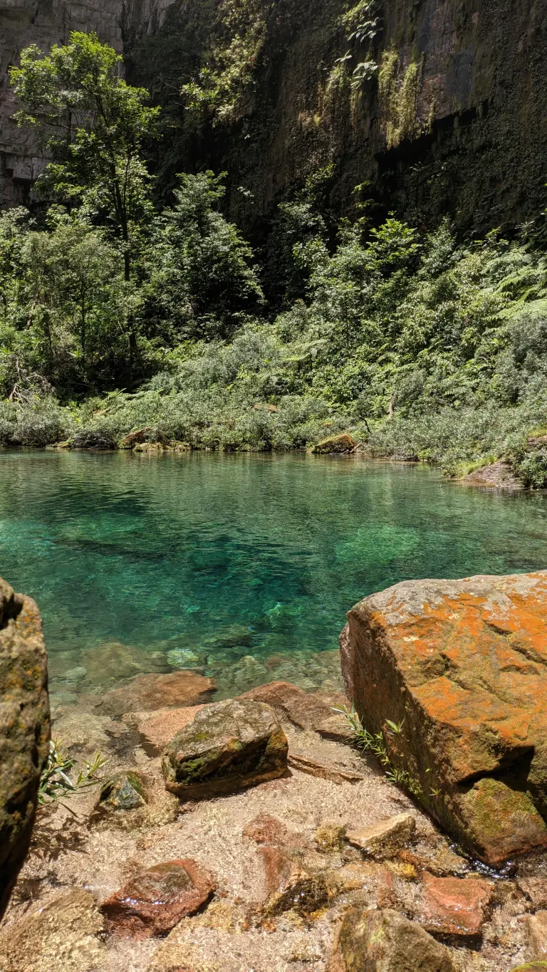 Vista vertical do Santuário das Araras com a água de tonalidade azulada e algumas rochas com um musgo laranja por cima