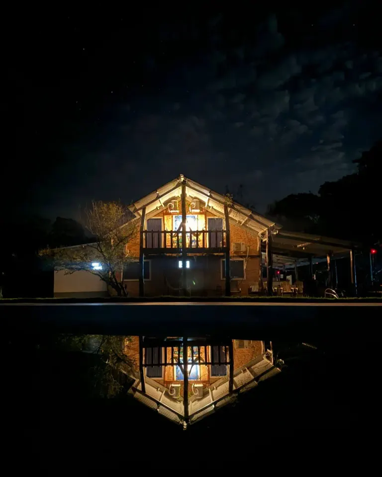 Sede da Fazenda Recanto da Serra iluminada à noite, com reflexo da casa na água em primeiro plano