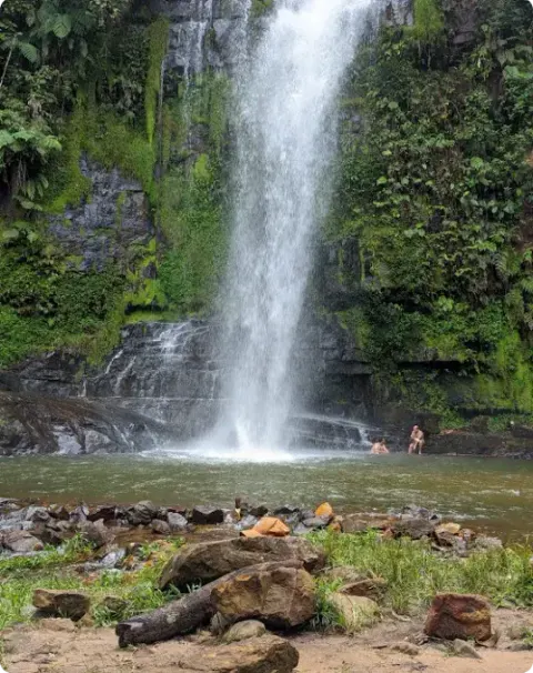 Visitantes desfrutando da Cachoeira Pé da Serra, posicionados nas pedras próximas à queda d'água.