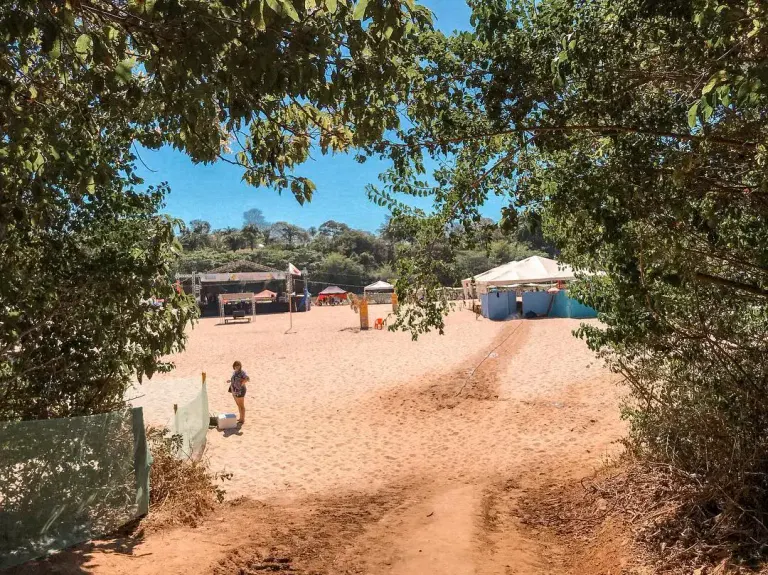 caminho de areia entre as árvores que leva à Praia da Arara, com uma tenda ao fundo