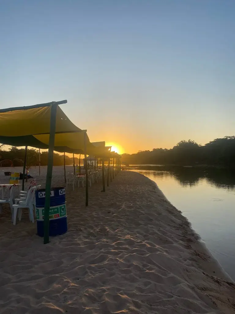 pôr do sol na Praia da Arara, com tendas de sombra na areia à beira do rio