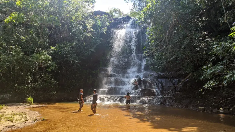 Visitantes se refrescando em uma das cachoeiras da trilha com queda d'água de aproximadamente 5 metros e formações rochosas em degraus naturais